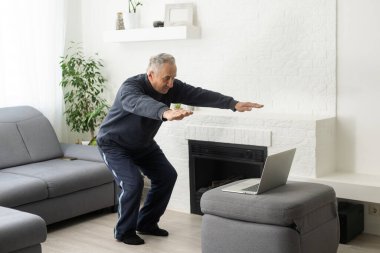 Gri saçlı son sınıf öğrencisi bir dizüstü bilgisayarla çevrimiçi eğitim yapıyor..