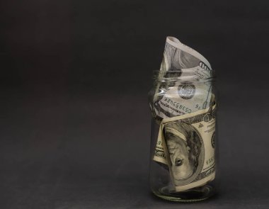 Bir dolarlık banknotlar arasında içi dolar dolu cam bir kavanoz. Gerçek para biriktirmenin kolay bir yolu..