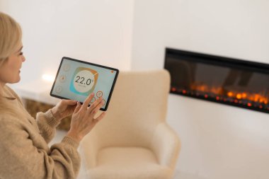 Beyaz oturma odasında uygulaması başlatılmış dijital tablet kullanarak akıllı ev aletlerini kontrol eden kadın. Akıllı ev kavramı.