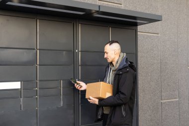 Depo Birimleri Bölümü. İnternette kiralık depolama üniteleri. Akıllı telefonu olan adam depoyu seçer. Web sitesinde depo kiralama. Kutuların yanında bir iş adamı. Arkaplanda bulanık depolama şirketi.