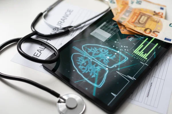 Modern social health insurance program. Tablet computer with healthcare application interface on screen. Stethoscope, x-ray image and cardiogram on wooden desk. Digital healthcare technologies.