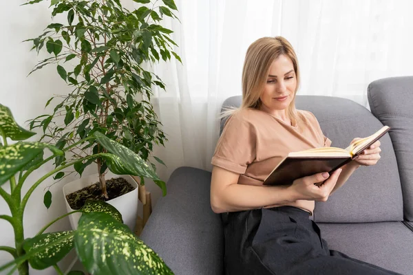 Mujer Rubia Leyendo Libro Mientras Está Sentado Sillón Beige Apartamento —  Fotos de Stock