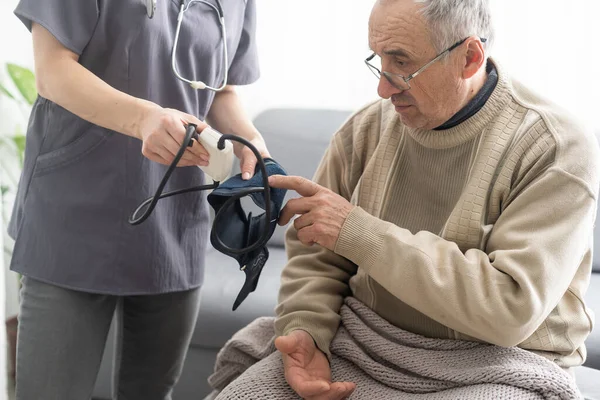 stock image Smiling young nurse taking old mans blood pressure.