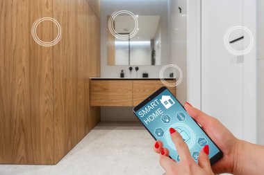 Akıllı ev telefonu, akıllı ev telefonu uygulama arayüzü cep telefonu ekranında, modern apartmandaki tüm ev sistemini telefonla kontrol eden genç bir kadın, konsept internet.