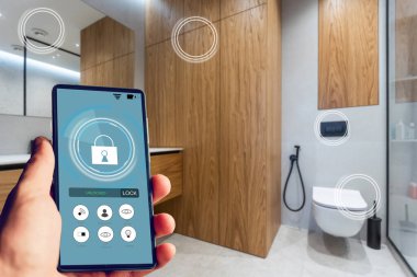 Akıllı ev otomasyon uygulaması arka planda ev içi olan kadın eliyle akıllı telefondan tutulan.