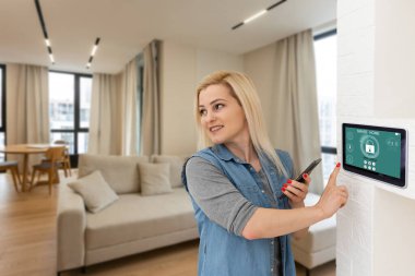 Akıllı ev sistemini kullanan ya da evden çıkmadan önce modern alarm sistemini çalıştıran hoş bir kadın. Mutlu kadın eve ya da daireye döndüğünde kolay güvenlik teknolojisini kapatıyor..