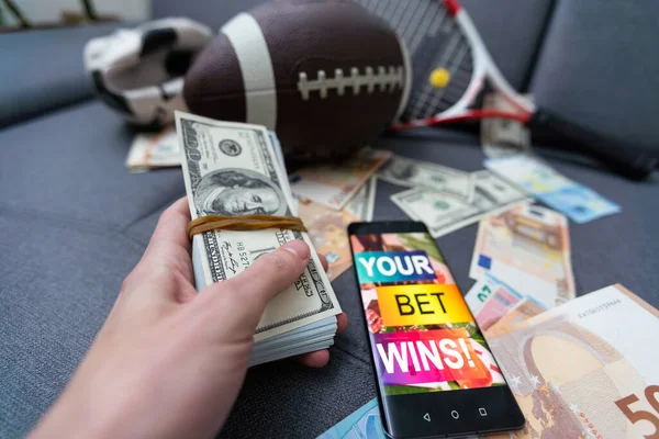 stock image Online sports betting. Dollars are falling on the background of a hand with a smartphone and a soccer ball. Creative background, gambling