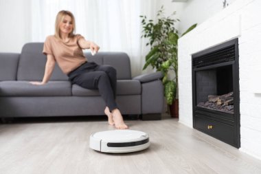 Dinlenen kadının olduğu koltuğun yanındaki modern robot elektrikli süpürge..