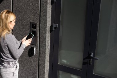 Akıllı ev kavramı - kadına yakın çekim - Elektronik kilit açmak için cep telefonu kullanın.