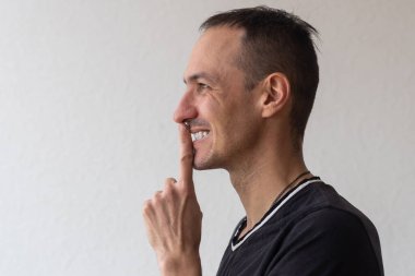 Dudaklarının yanında sakal tutan, sırlarını saklayan, sürpriz hazırlayan olumlu gülümseyen bir adam. Beyaz arka planda izole edilmiş kapalı stüdyo görüntüleri