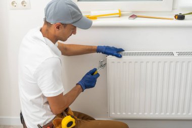 Erkek bir tesisatçı bir apartmanın ısıtma sistemine radyatör yerleştiriyor. Tulumlu ve ingiliz anahtarı olan bir adam..