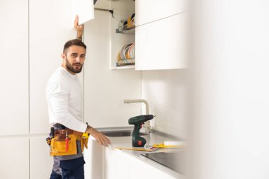 Two handymen, workers in uniform fixing, installing furniture and equipment in the kitchen, using screwdriver indoors. Furniture repair and assembly concept