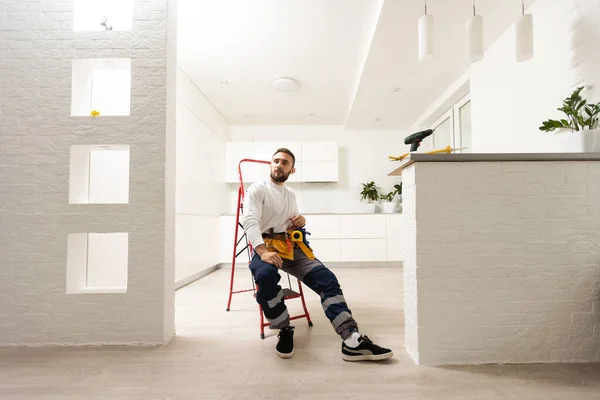 房屋维修 带有金属梯子的专业男性修理工的肖像 身穿工作服 面带微笑的人站在房间中央 在那里他已经完成了修理工作 — 图库照片