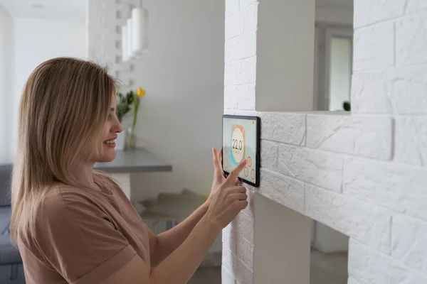 Controlling home with a digital touch screen panel installed on the wall in the living room. Concept of a smart home and mobile application for managing smart devices at home.