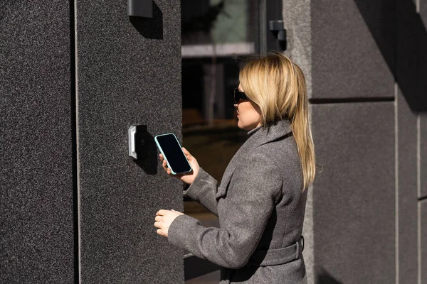 female entering secret key code for getting access and passing building using application on mobile phone, woman pressing buttons on control panel for disarming smart home system.