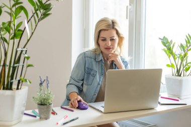 Çekici mutlu genç kız öğrenci ders çalışıyor, masada oturuyor, dizüstü bilgisayar kullanıyor, görüntülü sohbet ediyor, el sallıyor..