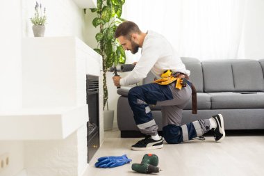 Professional technician sealing electric fireplace near white wall in room.