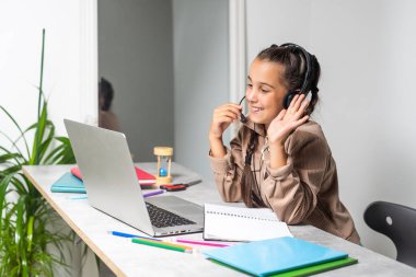 E-Learning. Shocked Little Schoolgirl Looking At Laptop Wearing Headphones Looking At Computer Web Camera In Shock Making Video Call And Learning Online At Home. Shocking News Concept