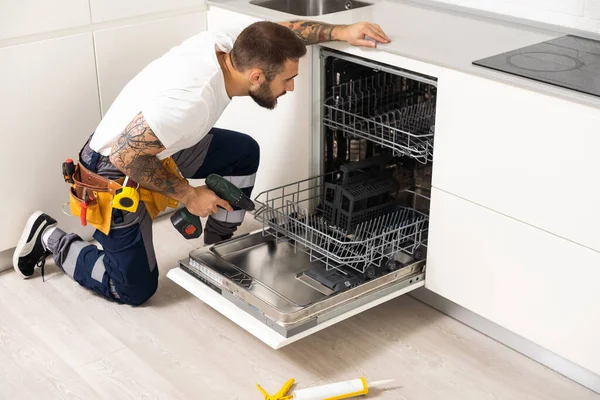 Man repairing a dishwasher with tools.