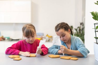 İki güzel kız kardeş, ahşap bir masada lezzetli pastalar süsleyip yiyorlar..