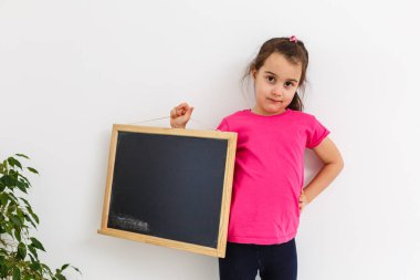 Smiling Little School Girl Holding Blank Chalk Board with Copy Space.