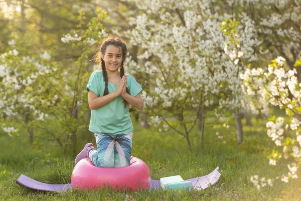a little girl does yoga lying on a sports mat in the park. a healthy lifestyle is a childish habit.