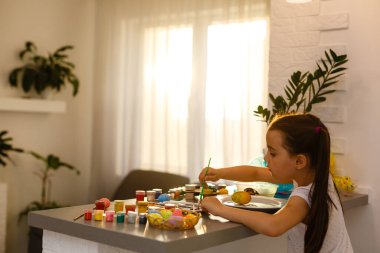 Şirin küçük kız fırçayla yumurta boyuyor. Paskalya konsepti