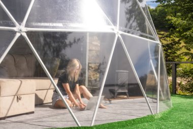 Kubbe kampında dizüstü bilgisayar kullanarak internette sohbet eden mutlu genç bir kadın. Glamping tatil konsepti.