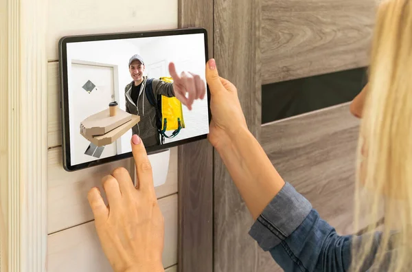 stock image Delivery man ringing door bell on cctv secure camera system on tablet app.