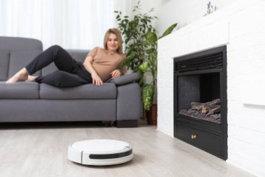 Dinlenen kadının olduğu koltuğun yanındaki modern robot elektrikli süpürge..