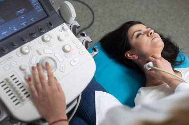 Doktor, bir kadının tiroidini incelemek için ultrason cihazı kullanıyor.
