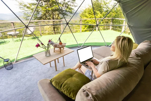 Young caucasian woman using and watching on laptop computer on in dome camping hotel. Tourism, vacation and weekend