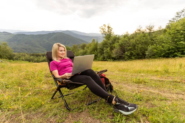 Young business woman working at the computer on the rock. Young girl downshifter working at a laptop at sunset or sunrise on the top of the mountain, working day