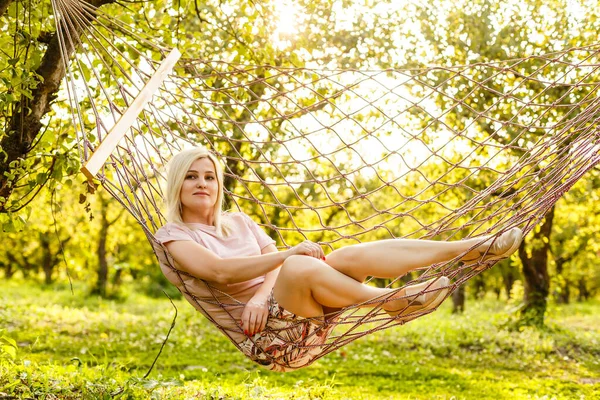 笑顔ブロンド女性リラックスオンザハンモックで庭 レジャー時間と夏休みのコンセプト — ストック写真