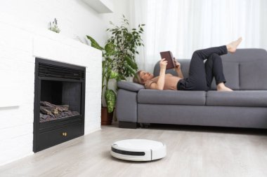 Kadın kanepede dinlenirken robot süpürgesi odayı temizliyor..