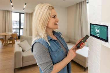 Akıllı ev sistemini kullanan ya da evden çıkmadan önce modern alarm sistemini çalıştıran hoş bir kadın. Mutlu kadın eve ya da daireye döndüğünde kolay güvenlik teknolojisini kapatıyor..