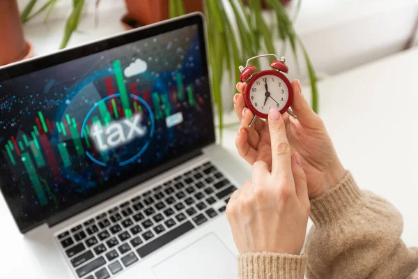 woman holds alarm clock near laptop and taxes.