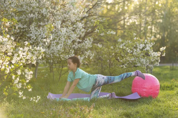 a little girl does yoga lying on a sports mat in the park. a healthy lifestyle is a childish habit.