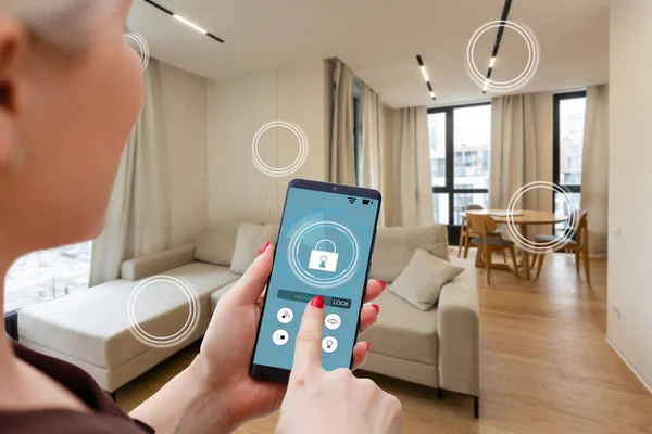 Home temperature, safety and environment control on mobile app. Smart phone in woman hand. Living room in background.