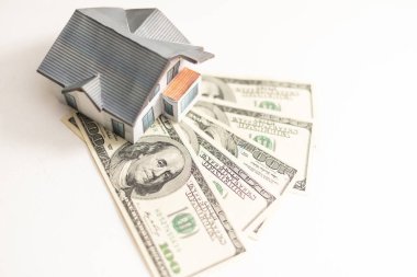 Küçük bir ev yüz dolarlık banknotlardan oluşan bir yelpazenin üzerinde yatıyor. Satın alınan evin anahtarları. Beyaz arka planda evin küçültülmüş kopyası. Yüksek kalite fotoğraf