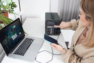 Woman inserting plug of portable solar station into socket at home.