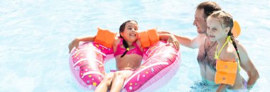 Aktif bir baba çocuklarına tropik tatil köyünde havuzda yüzmeyi öğretiyor. Yaz tatilleri ve spor konsepti.