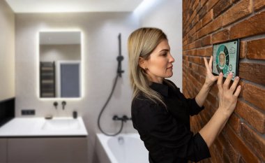 Akıllı ev sistemini kullanan ya da evden çıkmadan önce modern alarm sistemini çalıştıran hoş bir kadın. Mutlu kadın eve ya da daireye döndüğünde kolay güvenlik teknolojisini kapatıyor..