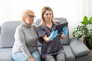 Ciddi pratisyen hekim, 70 'li yaşlardaki kadın hastaya tablet ekranı gösteriyor. Elektronik reçeteyi, tıbbi taramayı, muayene sonuçlarını, muayeneyi açıklıyor. Kadın ziyaretçi pratisyen