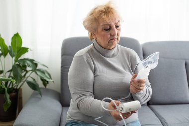 Nebulizör kullanan yaşlı bir kadın evde nefes alıp veriyor ve kameraya bakıyor..