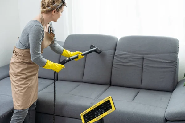 Woman cleaning couch with vacuum cleaner at home.