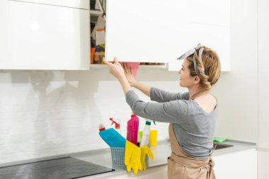 Hafta sonu ödevi. Genç ve güzel bir kadın evdeki rahat oturma odasını temizliyor. Parlak bir odada, ev kıyafetleri ve lastik eldivenler içinde güzel bir kadın.