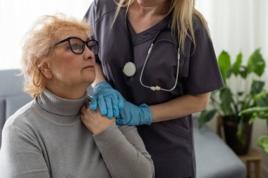 Bakıcı genç hemşire engelli ya da yaralı yaşlı kadının el ele tutuşmasına yardım ediyor. Sağlık sorunu olan yaşlı bir kadın engelli ve hastanede yürüyen bir kadın ile evde oturuyor.
