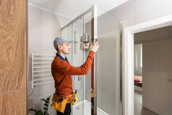 Professional handyman working in shower booth indoors.