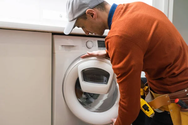 プロのツールボックスと労働者のスーツの若いハンサムな修理工は バスルームで洗濯機を固定しています — ストック写真